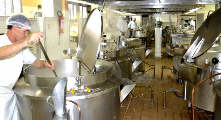 Foto: Denis Dias/PBH Cozinheiro prepara almoço em panela muito grande de retaurante popular. Ao lado e ao fundo, outras quatro panelas do mesmo tamanho e dois cozinheiros.