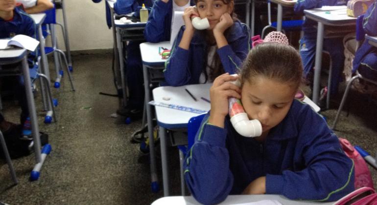 Professora de inglês adapta tecnologia norte-americana para incentivar e melhorar a leitura de estudantes em escolas da rede municipal. Foto: Lucienne de Castro Aluna da Rede Municipal de Ensino, sentada, testa "susurrofone", aparelho que permite que ela escute sua própria pronúncia.