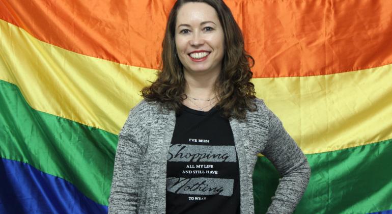 Analista de políticas públicas Elizabeth Matos Marques sorri tendo como fundo bandeira com as cores do arco-íris, símbolo do movimento LGBT.