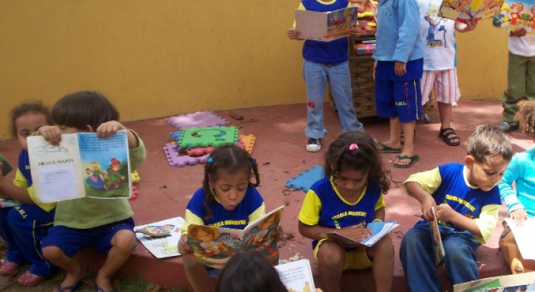 Dez crianças de idade entre 4 e 5 anos lendo livros infantis.