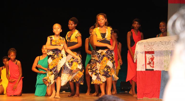 Cerca de 10 crianças em um palco, vestidas com roupas africanas