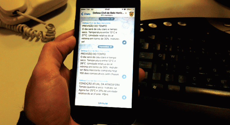 Defesa Civil cria canal do Telegram exclusivo para moradores, comerciantes e transeuntes da Avenida Vilarinho. Foto: Mônica Ramos/PBH Mão de homem segura celular com aplicativo Telegram da Defesa Civil.