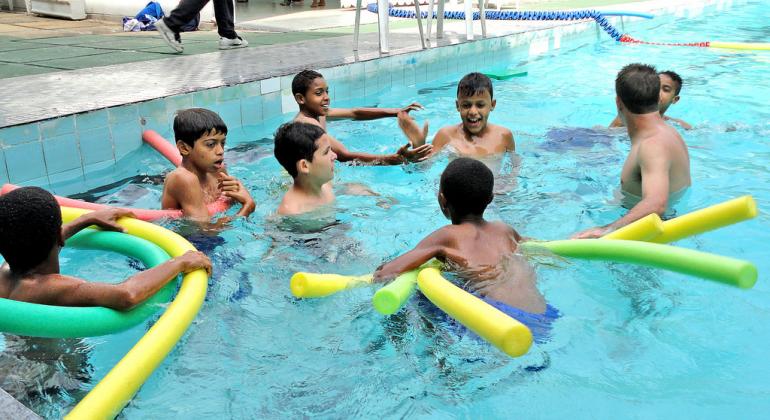 Programa Esporte Parceiro conta com aulas de natação Oito meninos estão na piscina brincando com boias