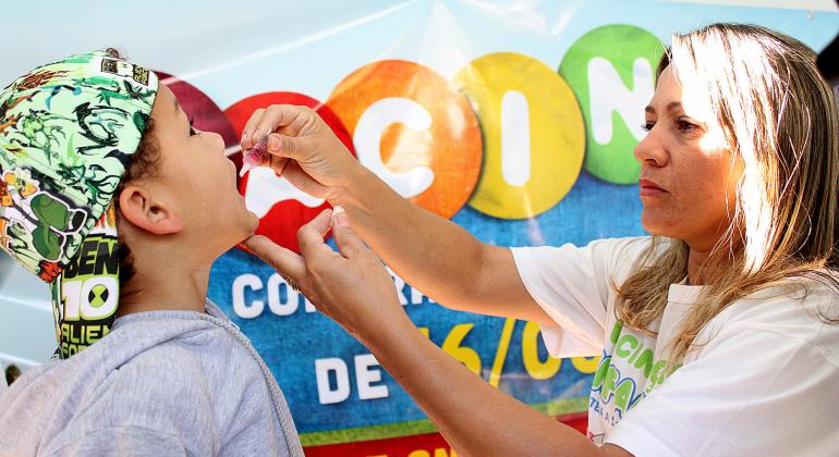 Servidora da saúde dá vacina da gotinha em menino de boné