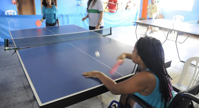 Duas garotas jogam pingue-pongue, uma delas é cadeirante.