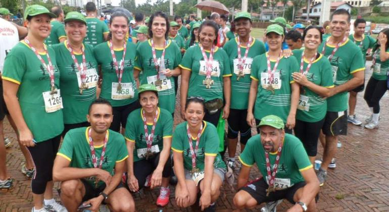 Incentivados por educadora física, usuários de Academia da Cidade da região Noroeste tornam-se adeptos de corridas de rua. Foto: Divulgação PBH Cerca de treze usuários da Academia da Cidade da região Noroeste com camisetas verdes e crachás, participando de uma maratona de corrida.
