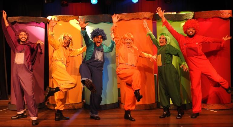 Teatro Marília apresenta, de 16/9 a 1º/10, aos sábados e aos domingos às 16h30, a peça infantil "Quem Roubou o Branco do Mundo?". Foto: Divulgação Seis atores, cada um vestido de uma das cores: roxo, amarelo, azul, verde, laranja e vermelho, dançam à frente de fundo colorido.