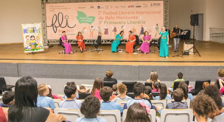 Com mais de 200 atrações, entre shows, mostras e oficinas, evento literário deste ano aposta na diversidade expressada pela literatura. Foto: Divulgação SMC/PBH Sete mulheres se apresentam em abertura do FLI BH com plateia com mais de doze pessoas assistindo.