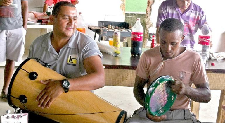 Ex-funcionário da SLU que realizou o sonho de concluir um curso superior é referência para os antigos colegas. Foto: SLU/PBH Foto de Gari engenheiro tocando instrumento de percussão ao lado de seu amigo, que toca pandeiro.