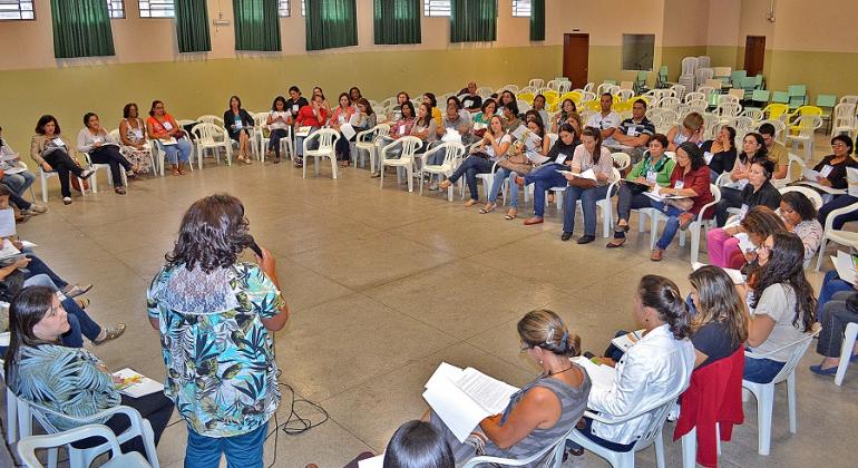 Foto: Divulgação PBH Mais de 50 pessoas reunidas, sentadas, em círculo, uma mulher, de costas, fala ao microfone. Imagem ilustrativa de edição anterior de Pré-Conferência de Políticas sobre Drogas na Regional Noroeste.
