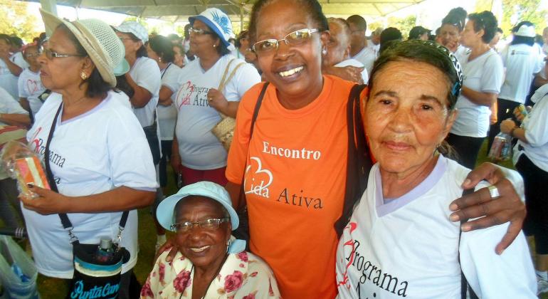 Quatro senhoras com a camiseta do Programa Vida Ativa; ao fundo, mais integrantes do programa. 