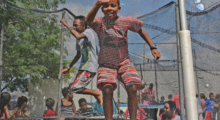 “BH é da Gente” leva lazer, cultura e esporte para as ruas Dois meninos brincam em cama elástica. Ao fundo, grupo de pessoas realiza outras atividades.