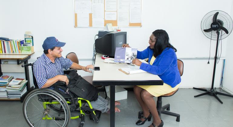 PBH participa do Dia D, mobilização nacional pela inclusão de pessoas com deficiência e reabilitados do INSS no mercado de trabalho. Foto: Laura Fonseca Cadeirante é atendido por mulher que está em mesa com computador e papéis.