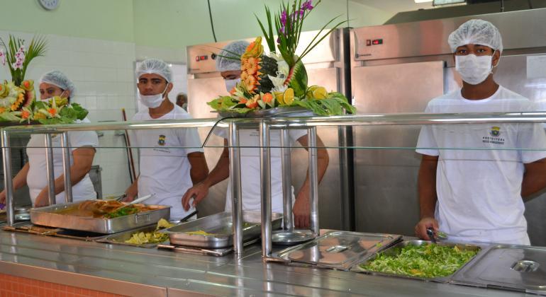 Confira os cardápios diários dos restaurantes populares de 25 a 29 de setembro. Foto: Divulgação/PBH Quatro funcionários do Restaurante Popular estão atrás do bufê para servir a comida