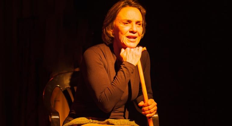 Frau Amália Freud. Foto: Solange Motta Atriz segura uma bengala sentada em uma cadeira.