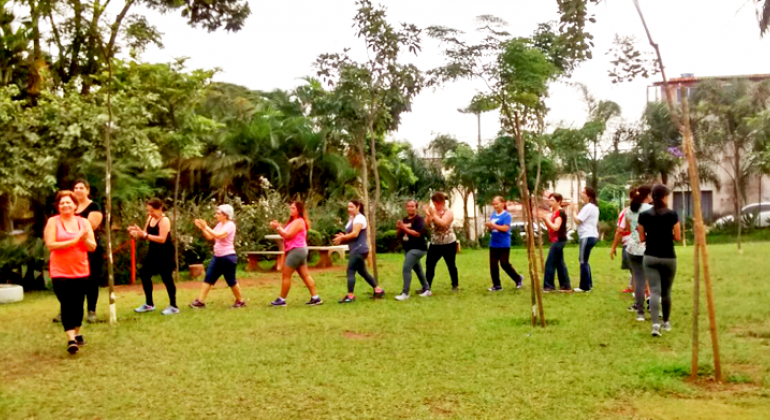Região Oeste conta com 8 unidades da Academia da Cidade, programa que oferece atividades físicas gratuitas com acompamento profissional. Foto: Divulgação PBH Cerca de treze participantes praticam atividade física em local aberto e com vegetação abundante.