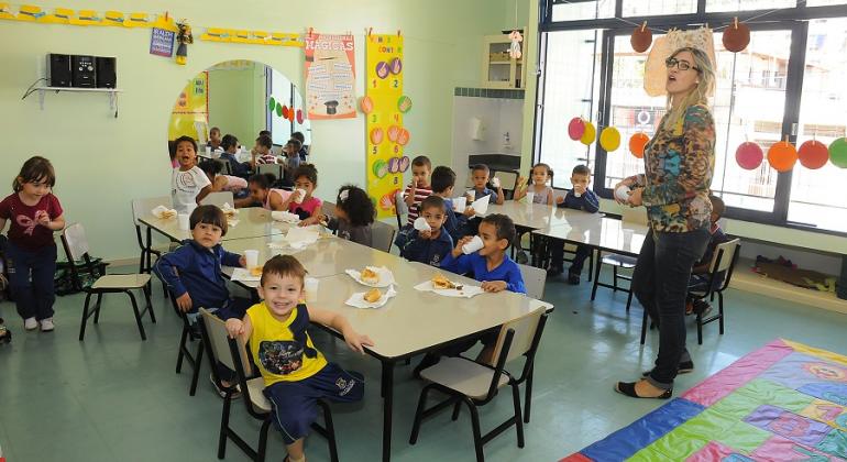 Educadora infantil acompanha o lanche de mais de dez crianças.