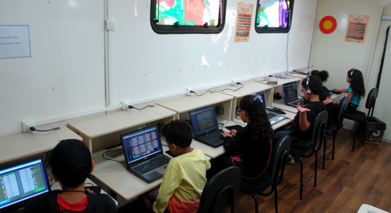 O Projeto Conexão Aberta será aberto no próximo sábado, dia 28, na Escola Municipal Presidente Itamar Franco, no Barreiro. Foto: Divulgação PBH Cinco crianças em frente a laptops dentro da Carreta do Conhecimento.