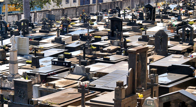 Muitos túmulos em cemitério municipal, durante o dia.