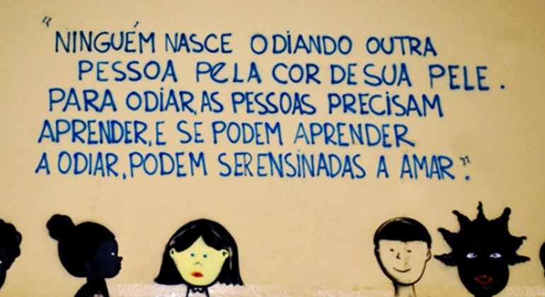 Fragmentos poéticos e frases de personalidades históricas inibem pichações e inspiram alunos de escola municipal no Barreiro. Foto: Kátia Gaspar/PBH Na parte de baixo de uma parede foram desenhadas quatro pessoas, duas delas negras, uma branca e uma com o rosto amarelo. Acima, os dizeres: "Ninguém nasce odiando outra pessoa pela cor de sua pele. Para odiar as pessoas precisam aprender, e se podem aprender odiar, podem ser ensinadas a amar.