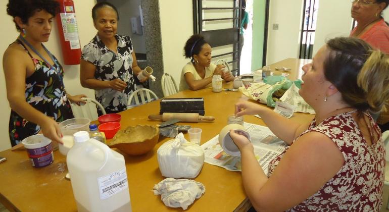 Com forno a lenha para queima de peças, Centro Cultural Venda Nova promove cursos de cerâmica. Foto: Avanilton de Aguiar Cinco mulheres pintam cerâmica em torno de uma mesa.