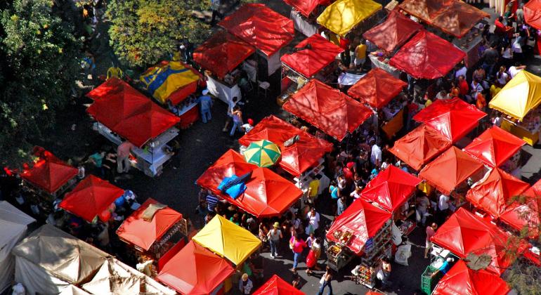 PBH, por meio da Regional Centro-Sul, realiza eleição da Comissão Paritária da Feira de Artes e Artesanato da Avenida Afonso Pena. Foto: Divino Advincula/PBH Vista aérea da Feira de Artes e Artesanato da Avenida Afonso pena, com cobertura das barraquinhas vermelhas em destaque e pessoas circulando entre elas.