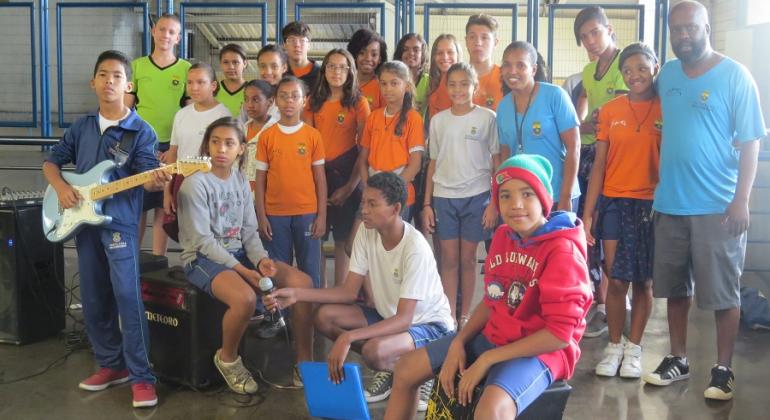 Projeto leva apresentações artísticas e culturais de alunos de 20 escolas municipais a diversos pontos da região Norte de BH. Foto: Yasmin Candelária/PBH Mais de vinte pessoas, uma delas com guitarra, juntas, em local coberto.
