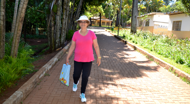 Senhora caminhando na calçada do Parque das Águas, muito verde ao redor.