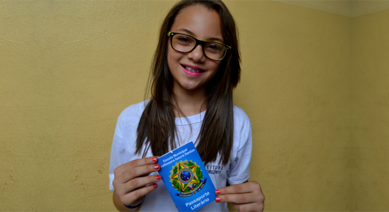 Escola Municipal Professora Isaura Santos estimula, nos alunos, o hábito da leitura e a reflexão sobre esta prática. Foto: Lidiane Sant'Ana/PBH Alune segura um passaporte para a leitura.