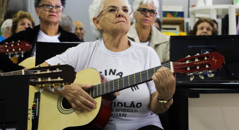 Prefeitura de BH apresenta o Diagnóstico do Idoso Idosa está sentada tocando violão