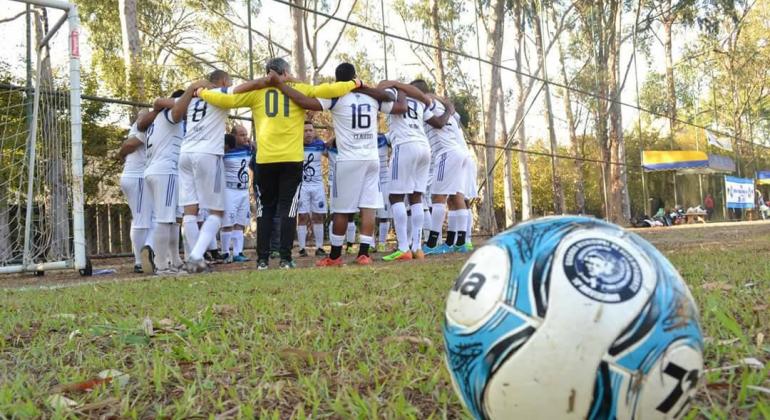 Equipe de futebol reunida no campo antes da partida ao lado da trave, à frente, bola de futebol. 