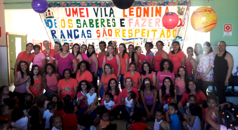 A UMEI Vila Leonina realizou evento de conscientização contra o câncer de mama e comemorou aniversário em outubro. Foto: Leandro Gomes Equipe de cerca de 40 pessoas da Umei Vila Leonida se veste de rosa para conscientizar a todos sobre a importância da prevenção do câncer de mama. Ao fundo, uma grande faixa com os dizeres: UMEI Vila Leonina: onde os saberes e fazeres das crianças dão respeitados.