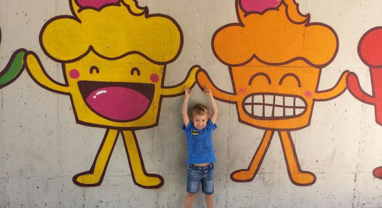 Criança 'dá as mãos' a dois bolinhos sorridentes pintados na parede.