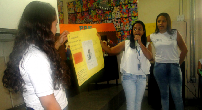 Escola municipal da região Leste utiliza personagens de mobilização da PBH em ação lúdica de combate ao mosquito Aedes aegypti. Foto: Naara Dias/PBH Três estudantes apresentam cartaz com cuidados para o combate ao mosquito mosquito Aedes aegypti.