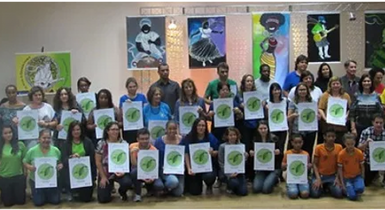Mais de vinte alunos com papéis em verde apresentam projeto de sustentabilidade.