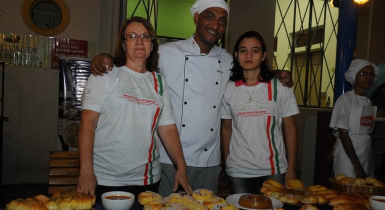 Duas alunas do Programa Pão Escola posam ao lado de professor. Foto ilustrativa.