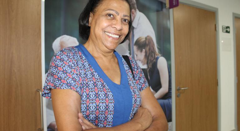 O recadastramento é obrigatório e deve ser feito no mês de aniversário do aposentado e do pensionista. Foto: Aline Pereira/PBH. Aposentada da Prefeitura de Belo Horizonte sorrindo, de pé, com os braços cruzados.