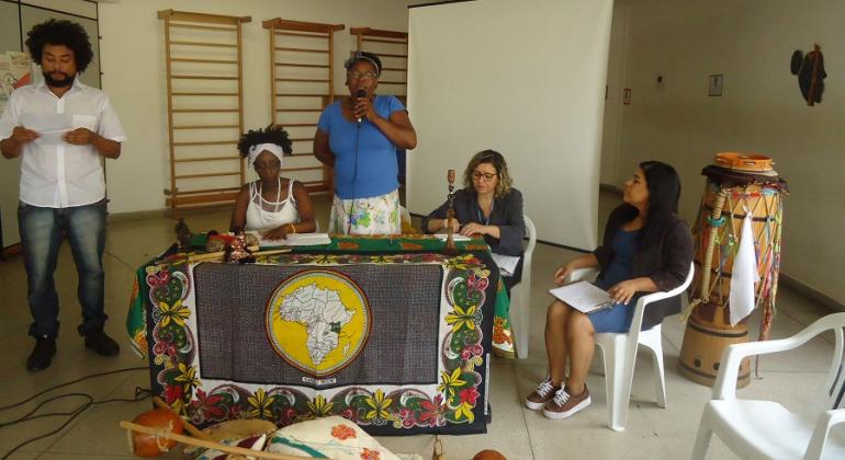 Cinco pessoas, com mesa com tambores e adereços afro, participam de Roda de Conversa sobre igualdade racial no Cras Lagoa.