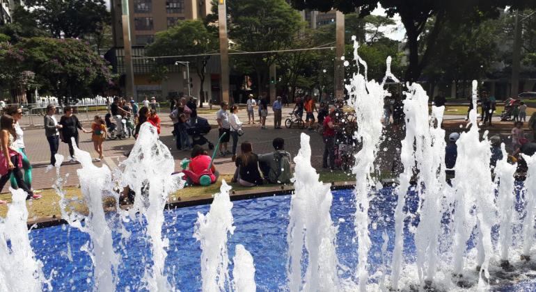 Pos trás da fonte de água da Praça da Savassi vemos ciclistas e passantes.