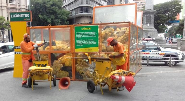 Lixo descartado no chão dos quatro quarteirões da Praça Sete de 11 a 13/12 alcançou o volume de 10 toneladas. Foto: Divulgação PBH Dois garis colocam lixo no lixômetro do centro de BH, que atingiram 10 toneladas em três dias.