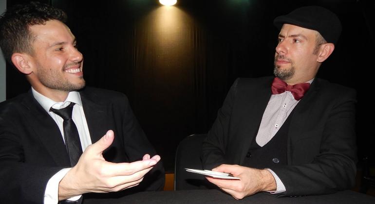 Os premiados mágicos Luiz Fosc e Fernando Às se encontram em um espetáculo de mágica que promete surpreender o público. Foto: Divulgação Dois mágicos interagem segurando um baralho.