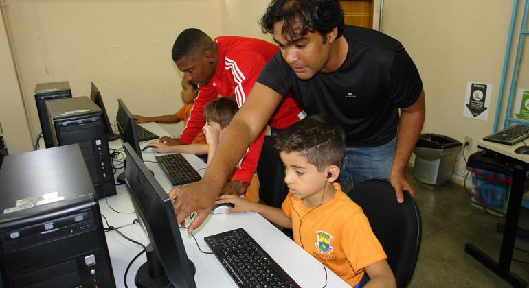 Cursos promovidos pela Prodabel para pessoas de todas as idades têm saldo positivo e serão ampliados em 2018. Foto: Divulgação PBH Dois técnicos da Prodabel ensinam duas crianças da Rede Municipal de Educação da PBH a acessar e utilizar computadores.