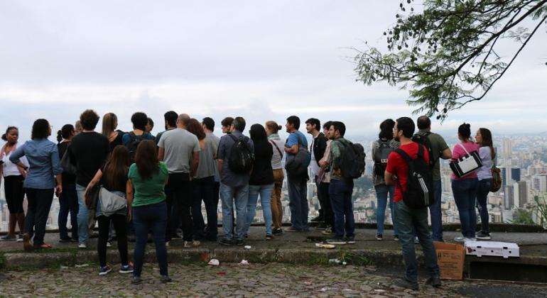 Prefeitura promove cursos e painéis de debate sobre mercados de solo e regularização de assentamentos até dia 8/12. Foto: Divulgação PBH Cerca de trinta pessoas, em mirante, observam a cidade de BH.