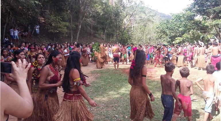 Mais de vinte índios da tribo Pataxó fazem círculo, junto a alunos de escola municipal.