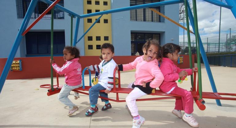 Quatro crianças de até 3 anos brincam em brinquedo de playground. 