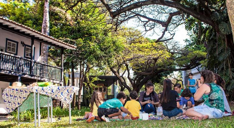 Visitas guiadas revelam a história de Belo Horizonte e atraem cada vez mais pessoas ao Museu Histórico Abílio Barreto. Foto: Ricardo Laf/PBH Cerca de sete crianças e um adulto fazem piquenique no gramado do Museu Histórico Abílio Barreto; ao fundo, casarão do museu.