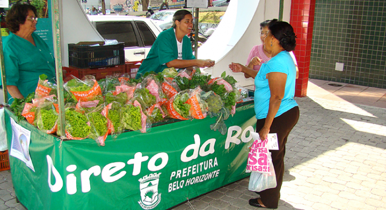 Duas mulheres observam alfaces em banca do Programa Direto da Roça.