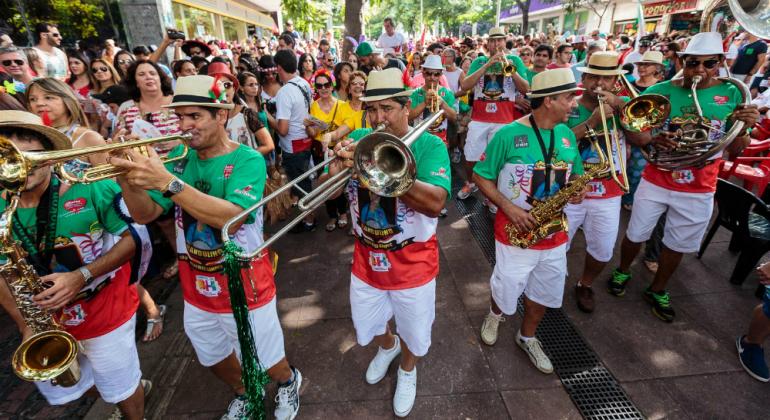 Pré carnaval de rua com bloco com mais de cinco instrumentistas seguido por multidão na rua.