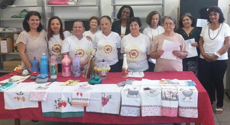Foto: Melissa Reis Onze mulheres, participantes d projeto Redescobrir, e os panos de prato decorados produzidos por elas.