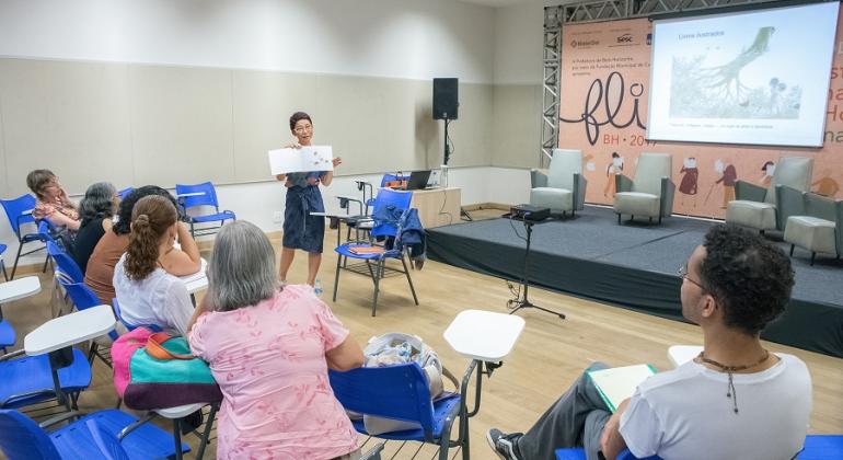 Mulher dá aula para quatro adultos, sentados em cadeiras.